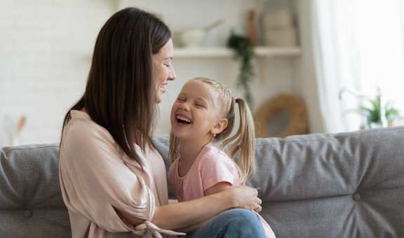 A woman and a girl are sitting on a grey couch.