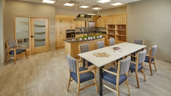 A dining room with a table and chairs and a kitchen in the background