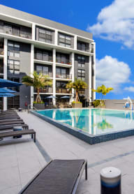 a large swimming pool with lounge chairs and umbrellas in front of a hotel