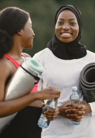 two women standing in a park holding water bottles