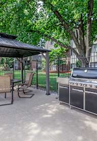 A patio with a grill and chairs under a canopy.