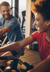 A man and a woman are working out on exercise bikes in a gym.