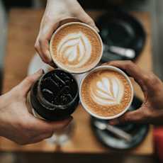 Three hands holding cups of coffee with latte art on top.