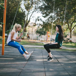 two women sitting on swings in a park