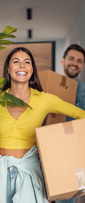 A woman is holding a potted plant and a cardboard box while a man carries another box.