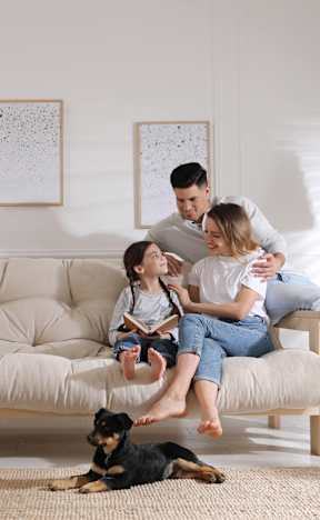 A family of three is sitting on a couch with a dog on the floor.