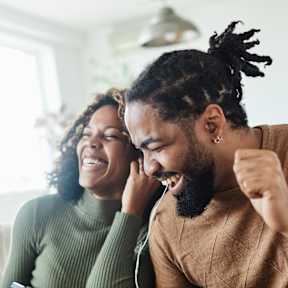 A man with dreadlocks is laughing while holding a phone to his ear.