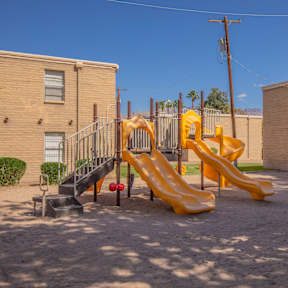 A playground with a yellow slide and a black slide.