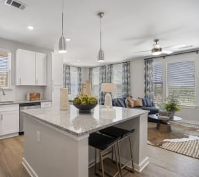 an open kitchen and living room with white cabinets and a marble counter top