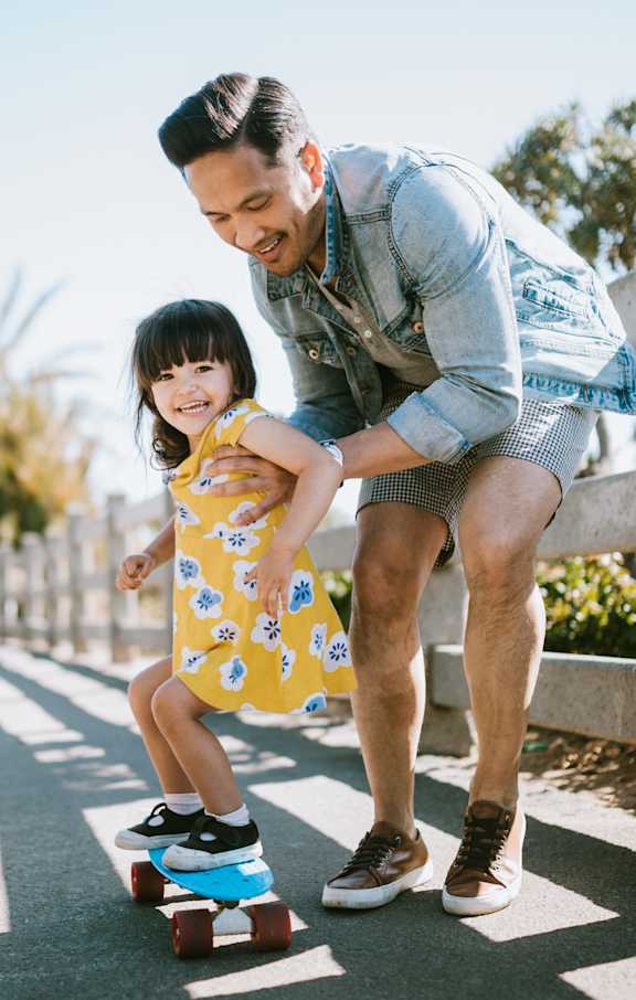 A man is teaching a little girl how to skateboard.