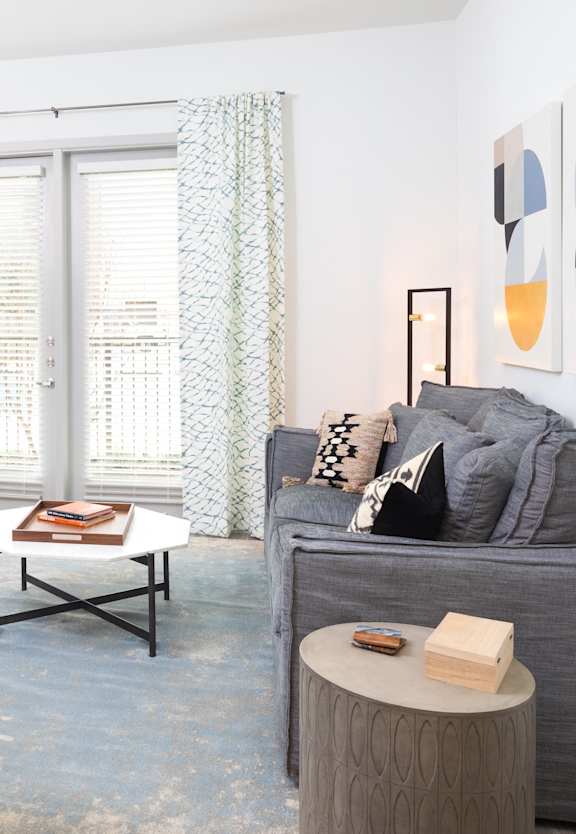 A living room with a blue armchair, a grey couch, a coffee table, and a painting on the wall.