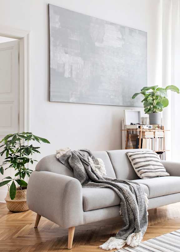 A living room with a grey couch, a potted plant, and a painting on the wall.