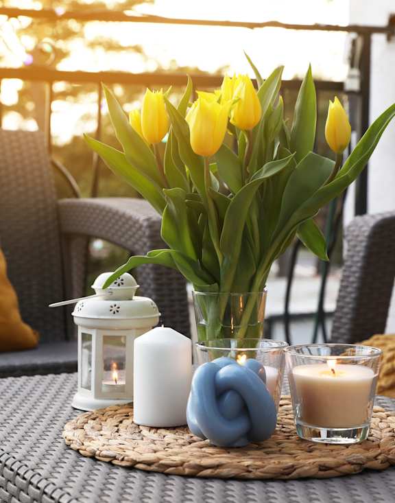 A table with a vase of yellow tulips, a candle, and a lantern on it.