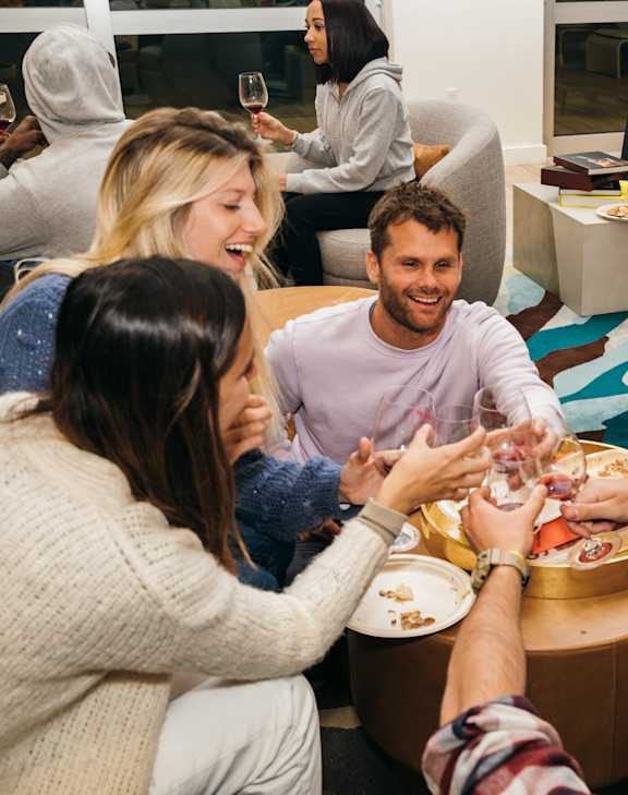 A group of people are gathered around a table, toasting with drinks in their hands.