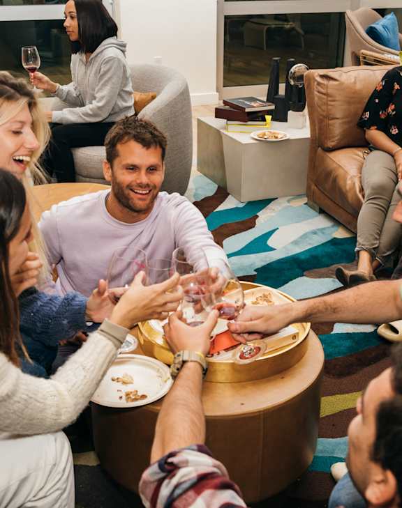 A group of people are gathered around a table, toasting with drinks in their hands.