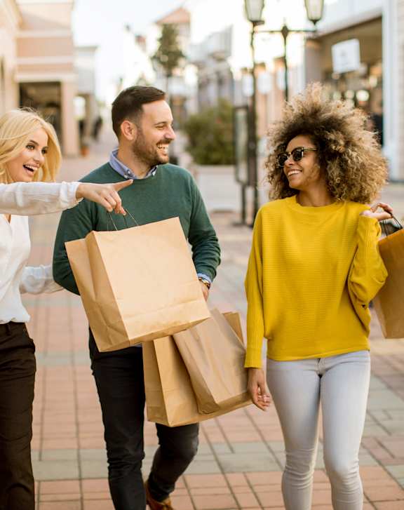 Three people walking down a sidewalk with shopping bags.