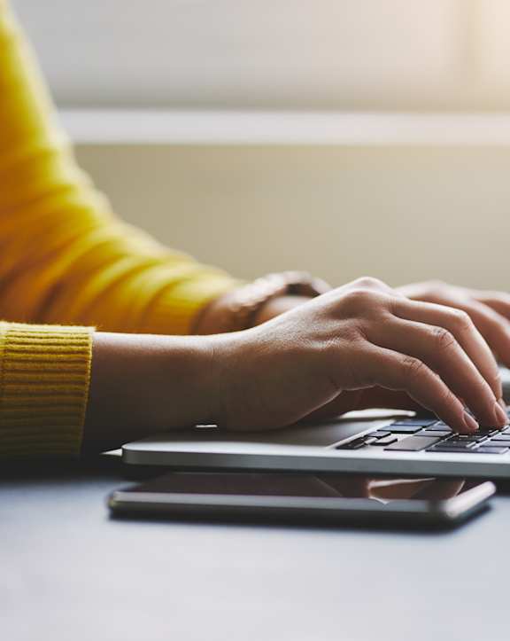 A person in a yellow sweater is typing on a laptop.