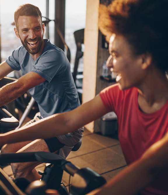A man and a woman are working out on exercise bikes in a gym.