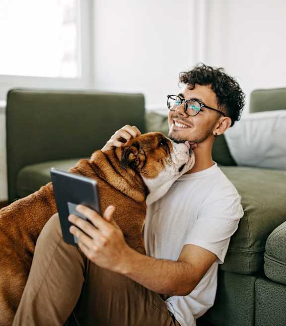 a man sitting on a couch holding a dog and looking at a tablet