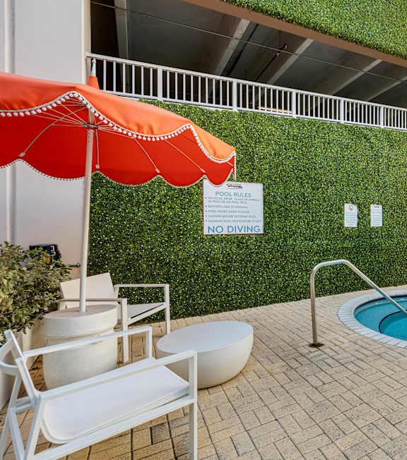 A pool area with a red umbrella and a green wall.