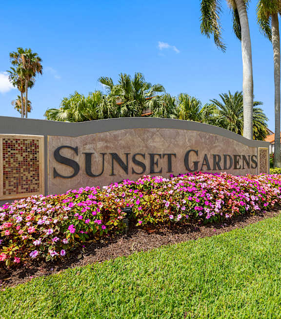 A sign that says Sunset Gardens in front of some flowers.