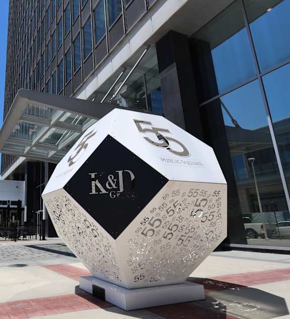 A large white and black sculpture with the letters K&D and the number 55 on it is in front of a building.