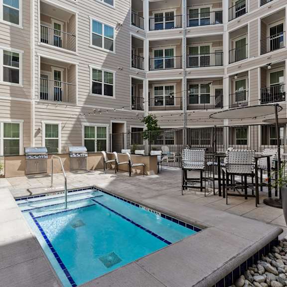 A small pool in a courtyard surrounded by chairs and plants.