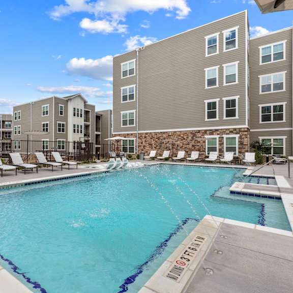 A swimming pool surrounded by lounge chairs and buildings.