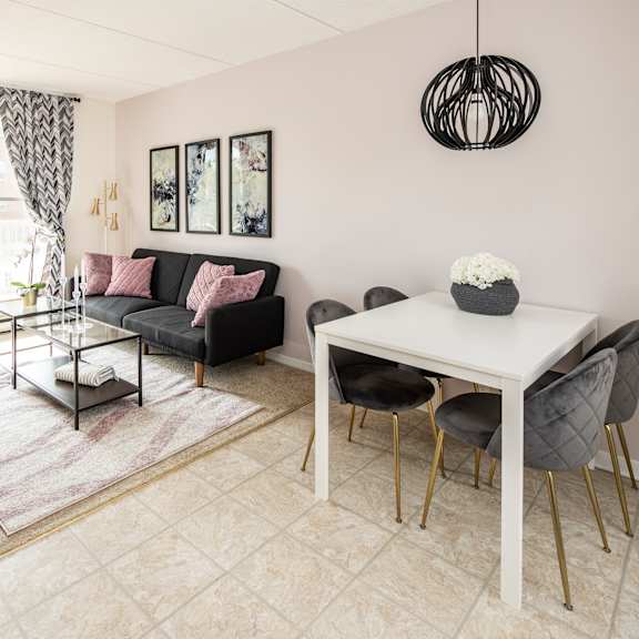 A living room with a grey couch, a white table, and a pink ottoman.
