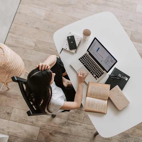 A woman is sitting at a table with a laptop and a book.