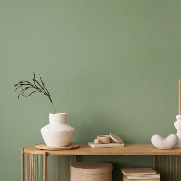 A white vase with a plant in it sits on a table with other decorative items.
