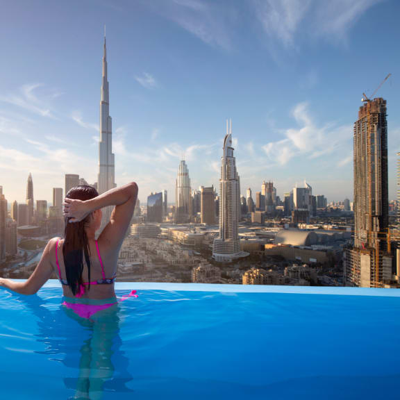 a woman in a infinity pool overlooking the dubai skyline