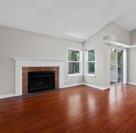 A large empty room with a fireplace and wood flooring.