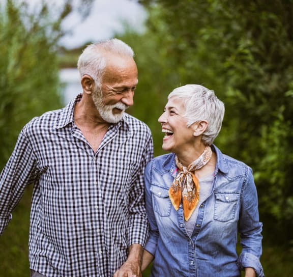an older man and woman walking in a garden laughing