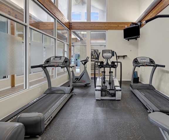 A spacious gym with cardio machines, windows, TVs, and weights at the Highlands Luxury Residences. 