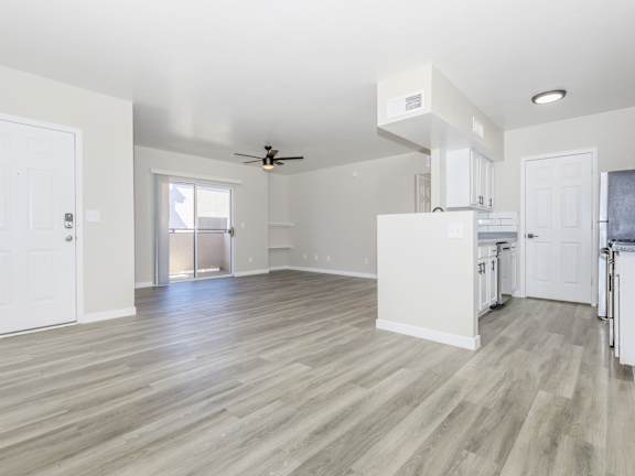 A spacious kitchen and living room with white walls and wood flooring.