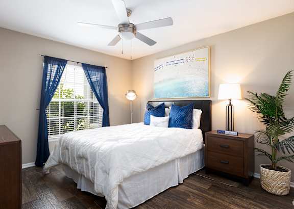A bedroom with a bed, nightstand, and a plant.