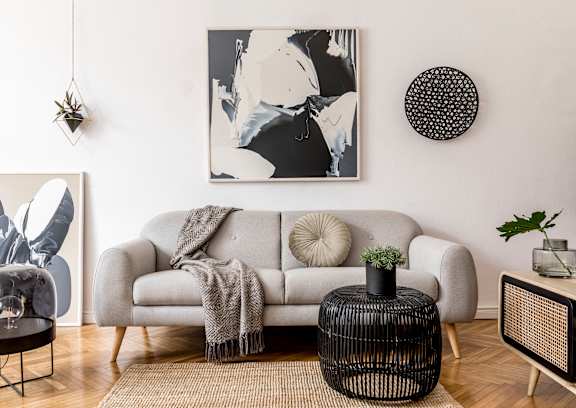 A living room with a grey couch, a glass table, and a black and white rug.