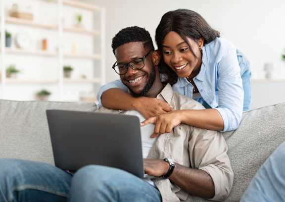 A man and woman are sitting on a couch with a laptop between them.