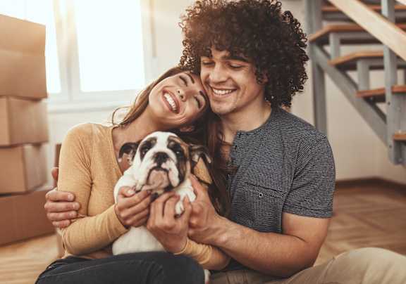 A couple is sitting on the floor with a dog in their arms.