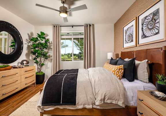 A bedroom with a bed, dresser, mirror, and plants.