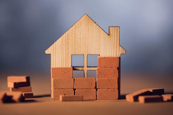 A house made of bricks is in the foreground with more bricks scattered around it.