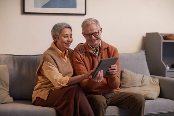 an older man and woman sitting on a couch looking at a tablet