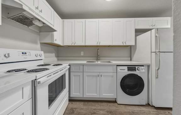 A white kitchen with a stove, oven, dishwasher, and refrigerator.