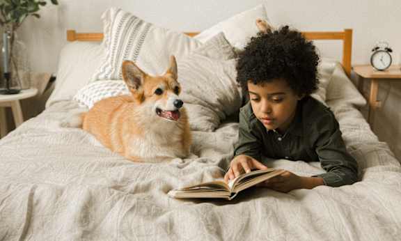 a boy and a dog laying on a bed reading a book