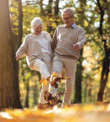 An older couple walking through the autumn leaves