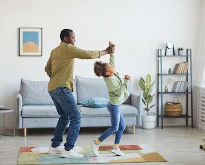 A man and a child are dancing together in a living room.