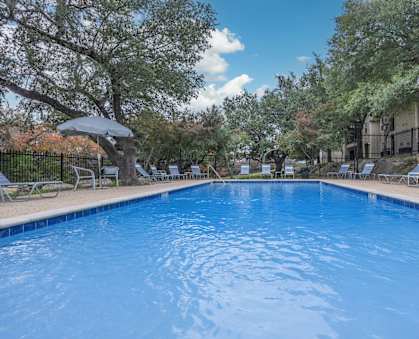 A swimming pool surrounded by trees and chairs.