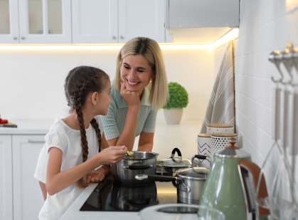 A woman and a girl are in a kitchen, the woman is smiling and the girl is looking at her.