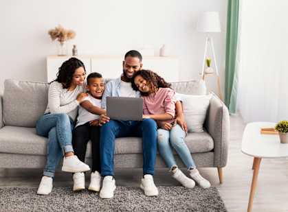A family of four is sitting on a couch looking at a laptop.